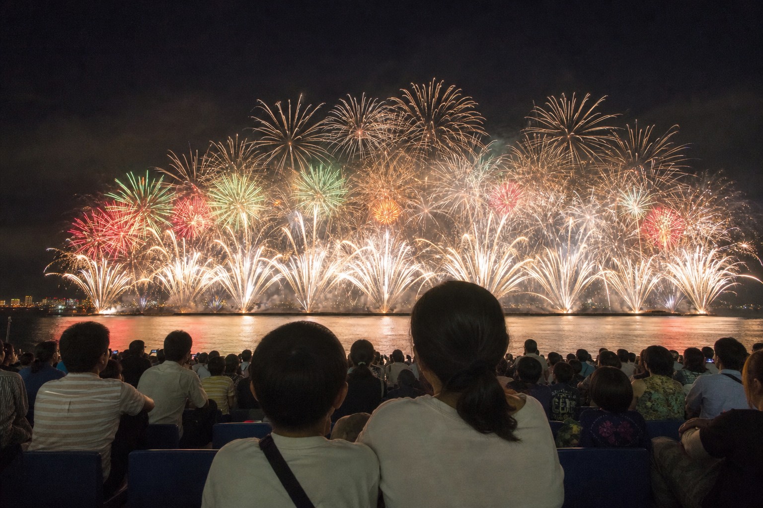 幕張の海辺で大規模な海上花火を眺める親子